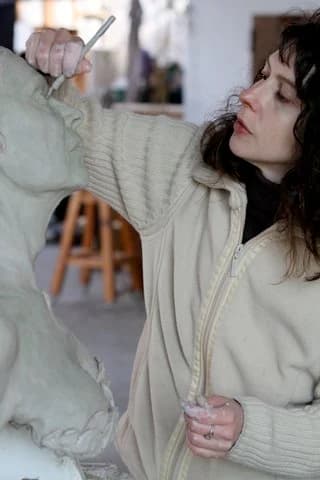 Lisa Silas working on a clay sculpture, modeling tool raised.