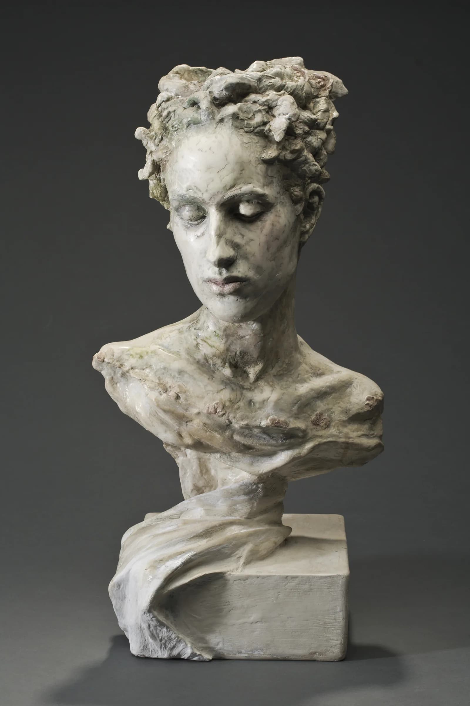 Sculpted bust of a young woman with her eyes lowered, mounted on a plain block.