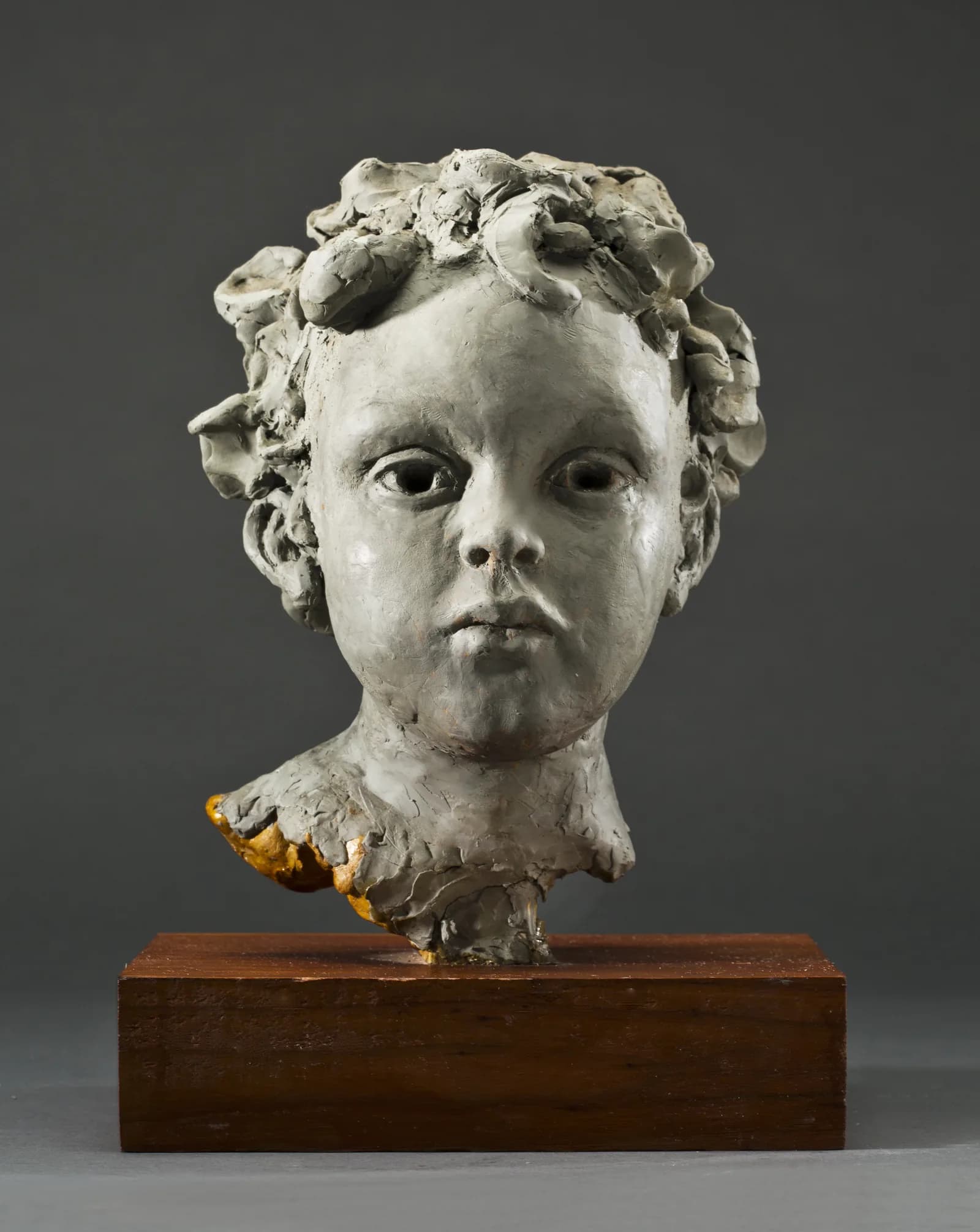 Sculpted head of a child with curling hair, on a wooden base.