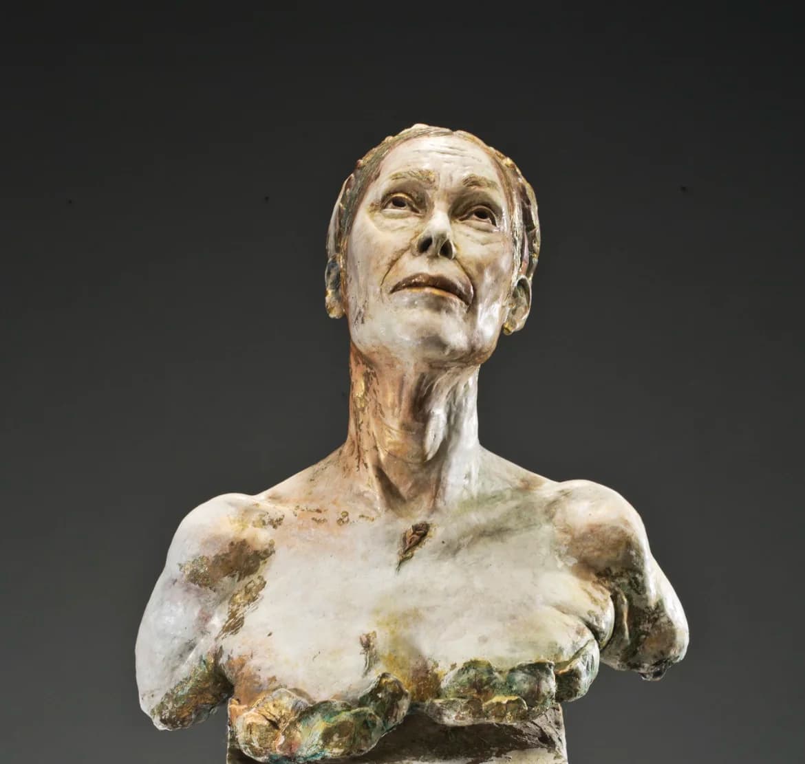 Sculpted female torso with a mottled green and ochre patina, broken off at the upper arms.